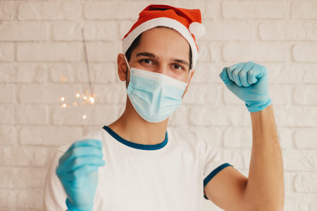 Male nurse in Santa hat, medical gloves, protective face mask show stay home message. Happy man doctor in face mask hold social awareness banner stay home in hands. Christmas self isolation campaignの写真素材