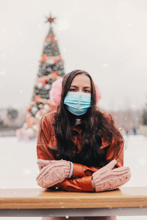 Portrait pretty young happy woman in stylish jacket, pink earmuffs skate on outdoor Christmas ice rink. Beautiful cheerful girl have fun and smile on ice skating rink. Winter holidays season activityの写真素材