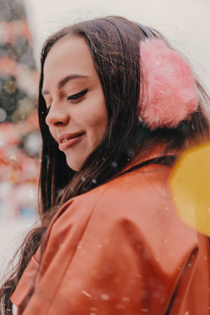 Portrait pretty young happy woman in stylish jacket, pink earmuffs skate on outdoor Christmas ice rink. Beautiful cheerful girl have fun and smile on ice skating rink. Winter holidays season activityの写真素材