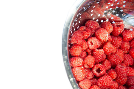 Delicious fresh and wet red raspberry in a colander for washing isolated at white background,...