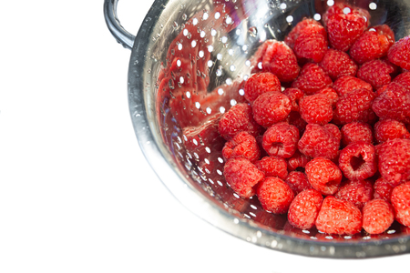 Delicious fresh and wet red raspberry in a colander for washing isolated at white background, closeup, detailsの写真素材