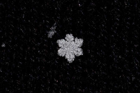 Macrophotography of a single snowflake on black textured background.の写真素材