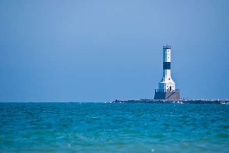 White lighthouse against blue sky and blue waterの写真素材