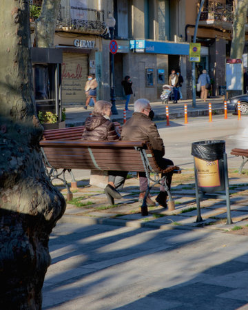 An older man and woman watch sitting on a bench in the street.の写真素材