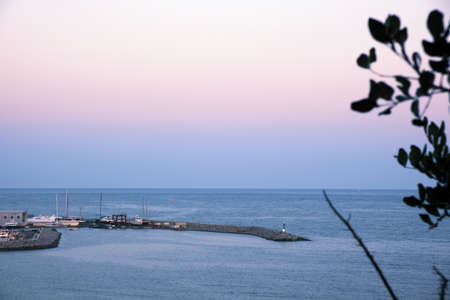 In the shot we see the breakwater and the lighthouse of the port of Arenys de Mar, Maresme, Barcelona, ââCatalonia. Sailboat sailing in the background.の写真素材