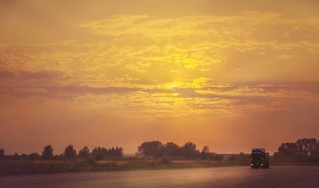 Truck traveling at sunset. Bright orange sky. Countryside road.の写真素材