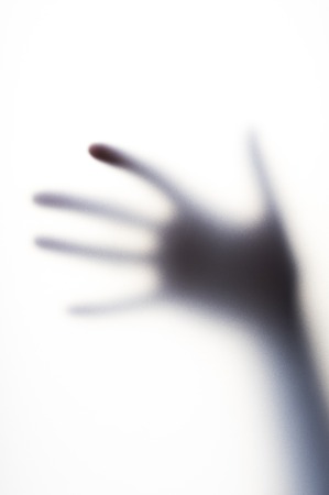 Diffused shadow of hand with thin fingers behind the frosted glass. Fear, phobia, danger or loneliness concept.の写真素材