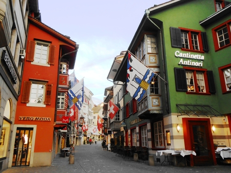 Zurich, Switzerland - April 17, 2014: People passing through a cobblestone street with low buildings, colorful facades, swiss flags and flags of the city of Zurich, Switzerland.のeditorial素材