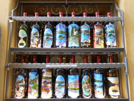 Bellagio, Italy â April 12, 2015: Hand painted wine bottles selling as souvenirs, exposed on the iron shelf on yellow facade in a street of Bellagio, Italy.のeditorial素材