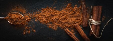 Ground cinnamon in teaspoon, and cinnamon sticks on dark background, top view, text spaceの写真素材