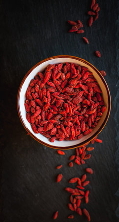 Dried goji berries in bowl on dark background, top view