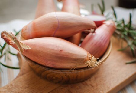 Close-up of shallots in a wooden bowl with fresh rosemary on cutting boardの写真素材