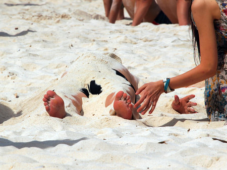 man buried in sand on the sand beach by young womanの写真素材