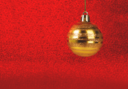 Hanging Christmas golden look ball on red glitter blurred background. Decoration concept. Copy space for your text.の写真素材