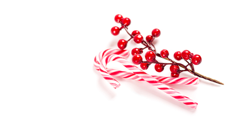Two Christmas candy canes with a branch of decorative berries on white background isolated.の写真素材