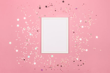 Festive background with blank white photo frame on pink pastel with scattered confetti. Mock up for...