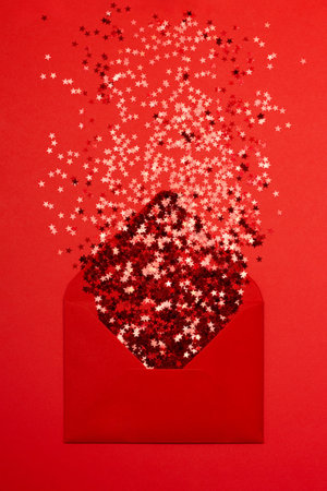 Red star shaped confetti pouring out of red envelope on red background. Flatlay style. Holiday or correspondence concept.の写真素材