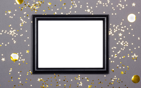 Festive background with blank black photo frame on gray with scattered golden confetti. Mock up for photo or text. Top view. Flat lay style.の写真素材