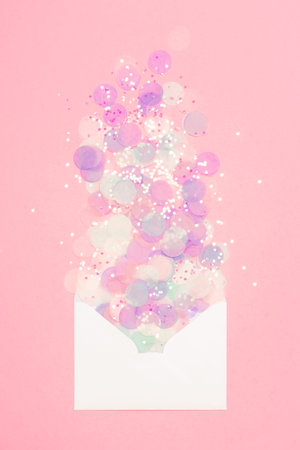 Sparkling confetti pouring out of white envelope on pastel pink background. Correspondence concept.