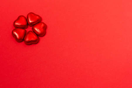 Chocolate heart shaped wrapped candies on red paper background. Minimal Valentines day background. Copy space for your text.の写真素材