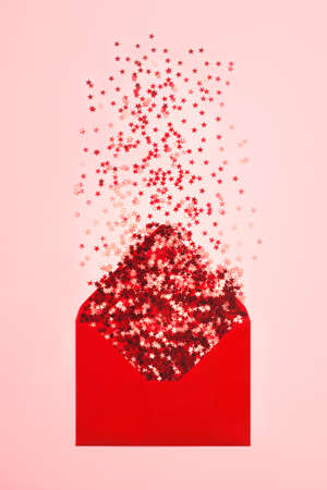 Red star shaped confetti pouring out of red envelope on pink background. Flatlay style. Holiday or correspondence concept.の写真素材