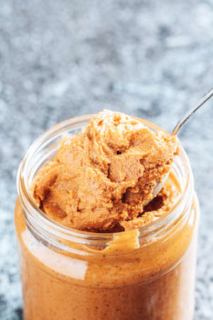 Spoon dipping into a glass jar with crunchy peanut butter.の写真素材