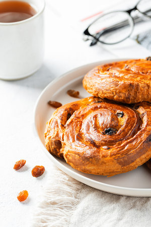 Breakfast scene. Raisin whirls on white plate and cup of tea. Danish pastry.の写真素材