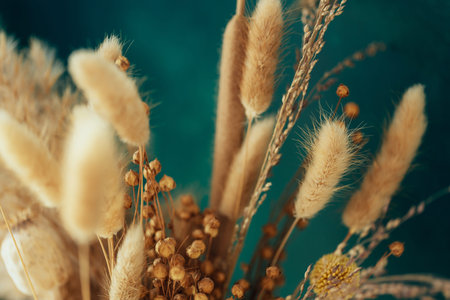 Bouquet of beige dried flowers on green-blue background.