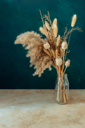 Bouquet of beige dried flowers in a glass vase on green-blue background.の写真素材