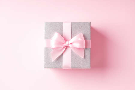 Silver glitter gift box with pink ribbon bow on pink background.の写真素材
