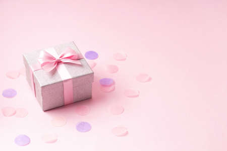 Silver glitter gift box with pink ribbon bow on pink background with confetti.の写真素材