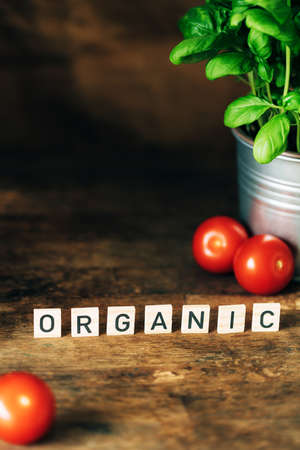 Dark wooden background with letters, pot of fresh basil and tomatoes.の写真素材