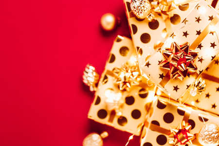 Gift boxes with golden bows, Christmas tree toys and lights on red background.の写真素材