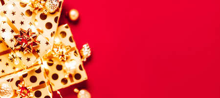 Gift boxes with golden bows, Christmas tree toys and lights on red background.の写真素材
