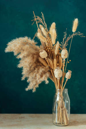 Bouquet of beige dried flowers in a glass vase on green-blue background.の写真素材