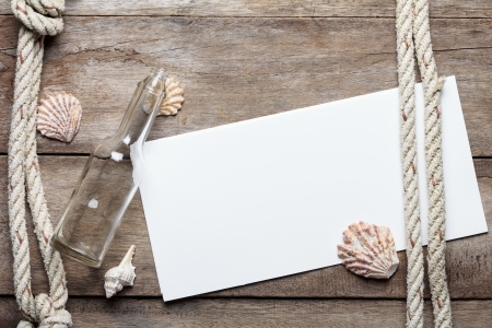 Blank paper sheet on weathered wood background with rope, shells, and bottleの写真素材