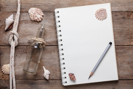 Weathered wooden table with blank notepad, pencil, rope and shellsの写真素材