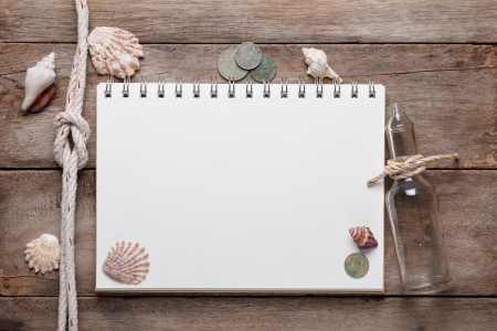 Weathered wooden table with blank notepad, coins and shellsの写真素材