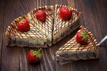 Slices of cheesecake with strawberry on wooden table, one on cake lifterの写真素材