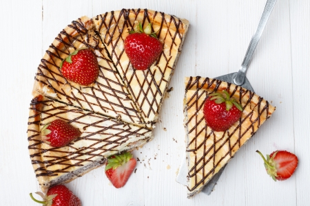 Slices of cheesecake with strawberry on wooden table, one on cake lifterの写真素材