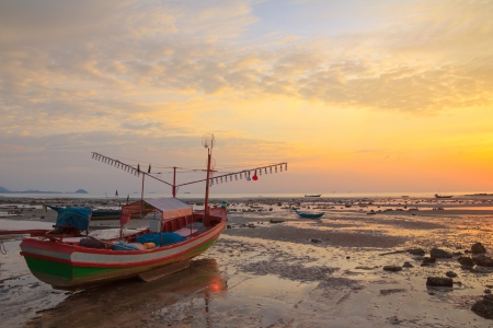 Small wooden boat with light bulbs for night squid fishing on the shore during ebb tide, Thailandの写真素材