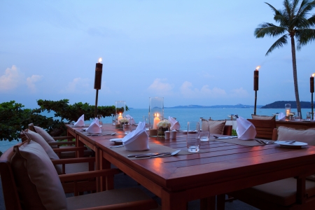 Romantic dinner setting at the beach on sunset, outdoor restaurant tablesの写真素材