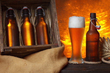 Beer glass with wooden crate full of beer bottles and wheat ears on tableの写真素材