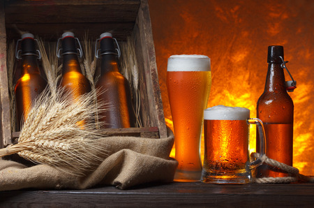 Beer glasses with wooden crate full of beer bottles and wheat ears on tableの写真素材