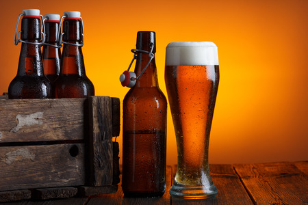 Beer glass with wooden crate full of beer bottles on tableの写真素材
