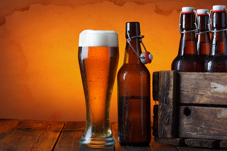 Beer glass with wooden crate full of beer bottles on tableの写真素材