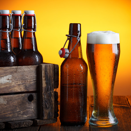 Beer glass with wooden crate full of beer bottles on tableの写真素材