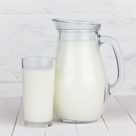 Milk glass and jar on white wooden tableの写真素材