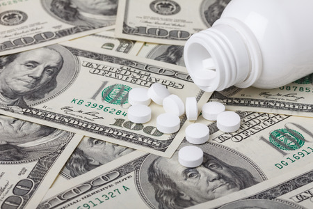 Pills and bottle on hundred dollar bills, medicine and health care cost conceptの写真素材