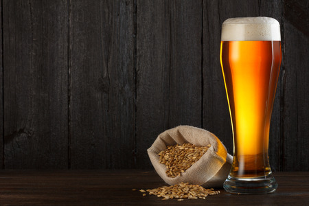 Beer glass with bag full of beer barley for brewing, on wooden table with copy spaceの写真素材